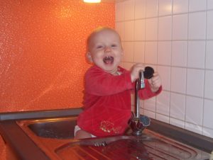 Baby sittzt in der Spühle und hat den Stöpsel entdeckt